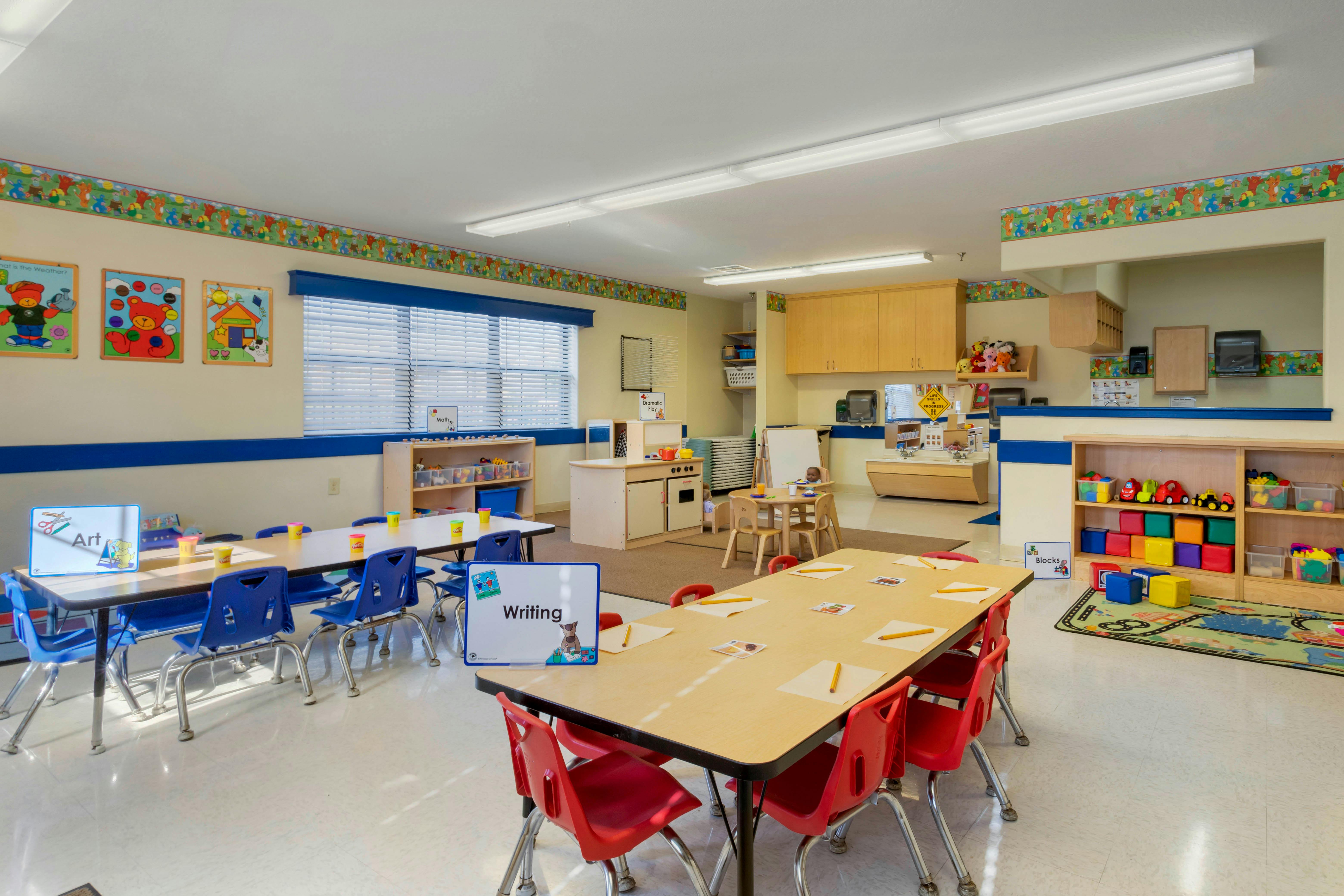 Classroom with child-sized tables and chairs, play kitchen, and toy shelves