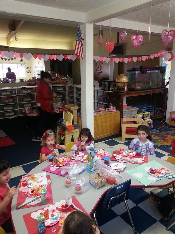 Children sitting at tables in a classroom eating snacks