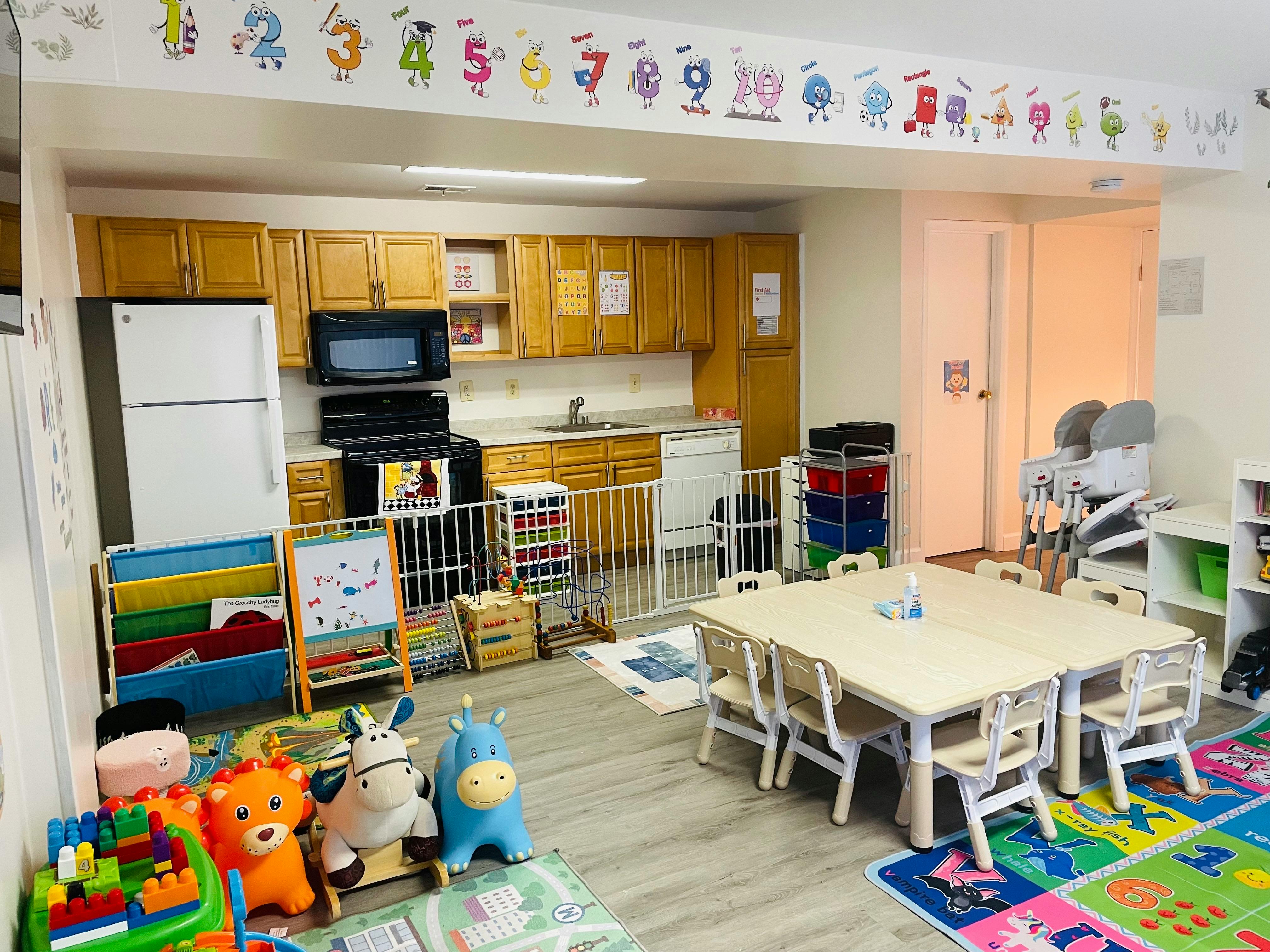 Childcare room with a kitchenette, small tables, chairs, and play equipment