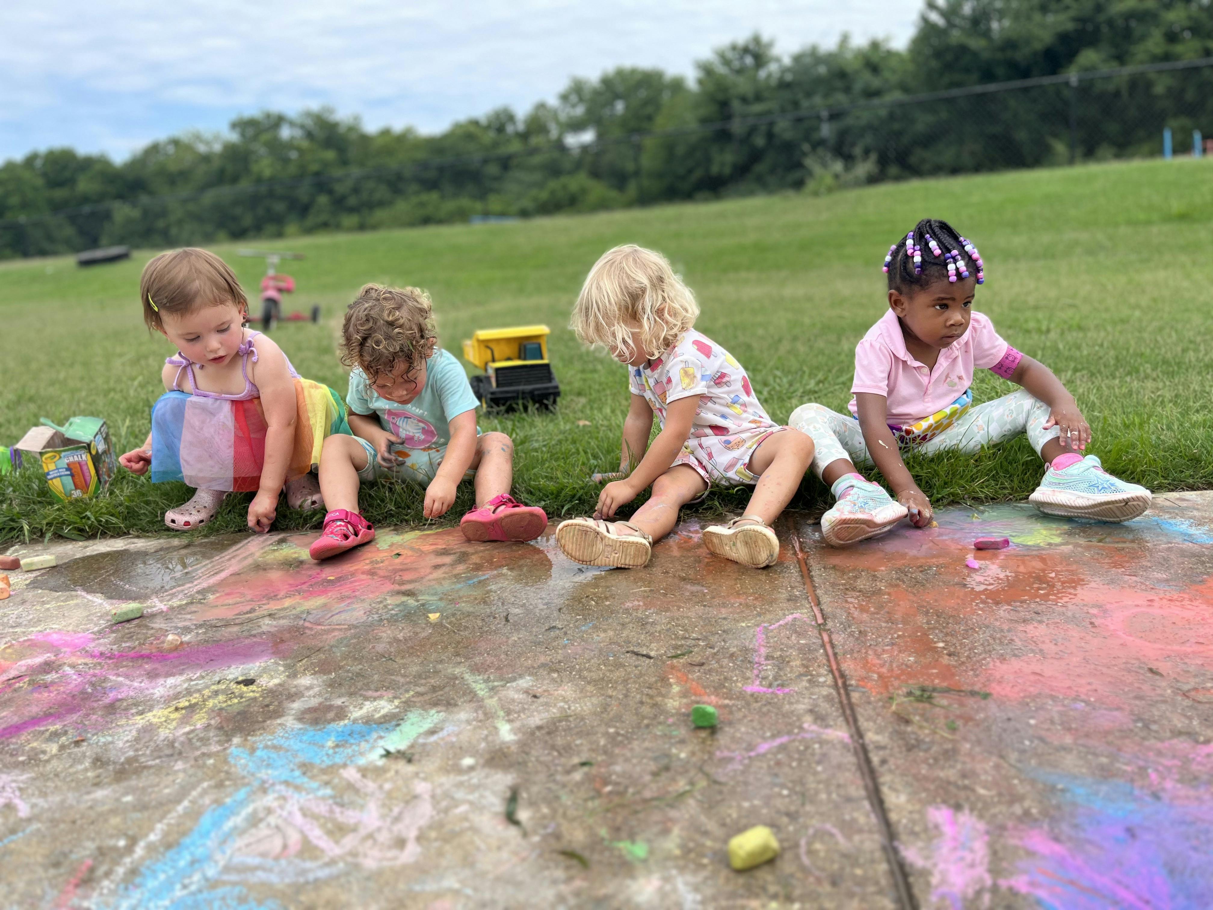 Four children sitting on the ground drawing with chalk on a patio
