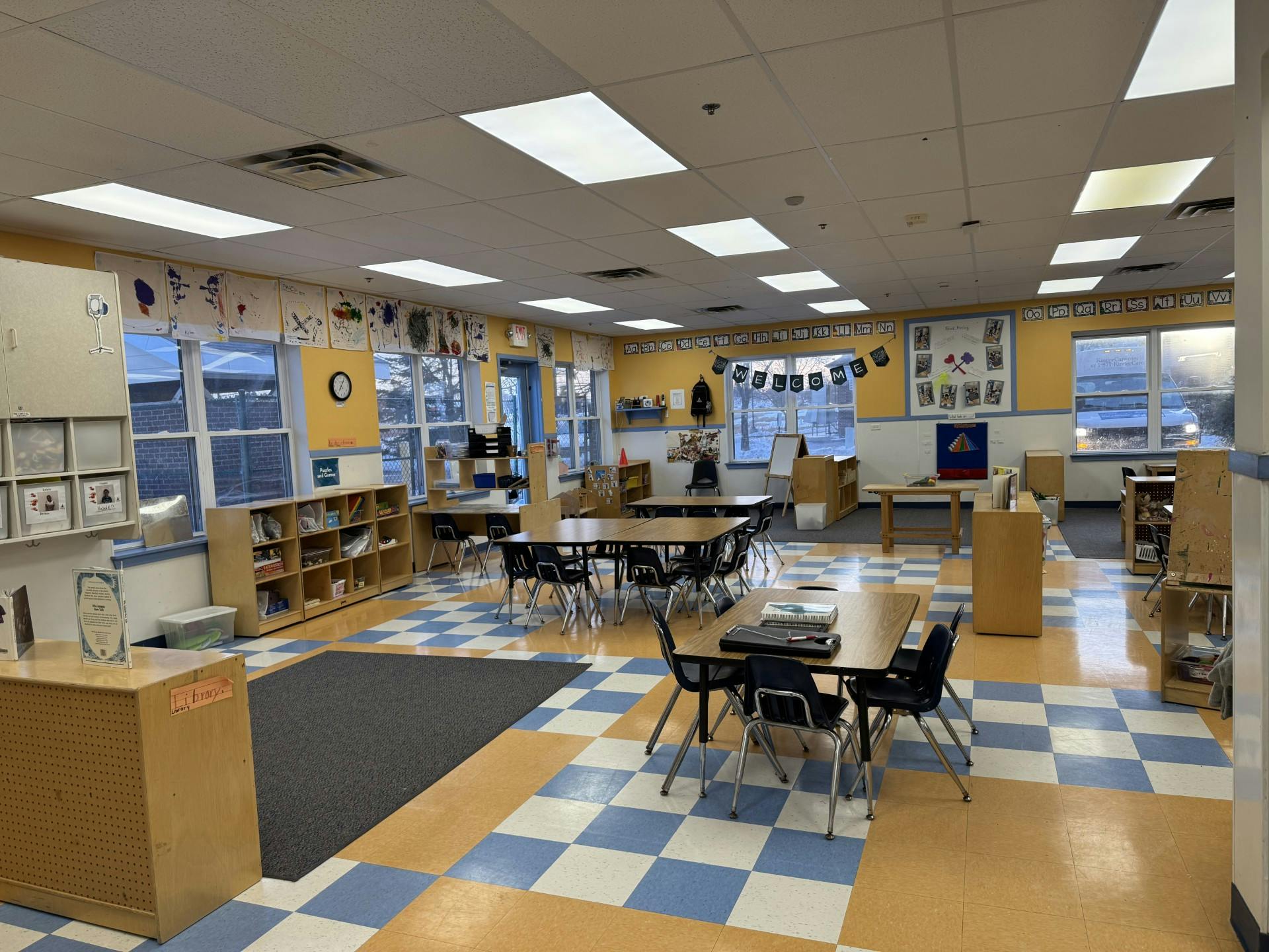 Empty classroom with tables and chairs, bright yellow walls, and checkerboard floor
