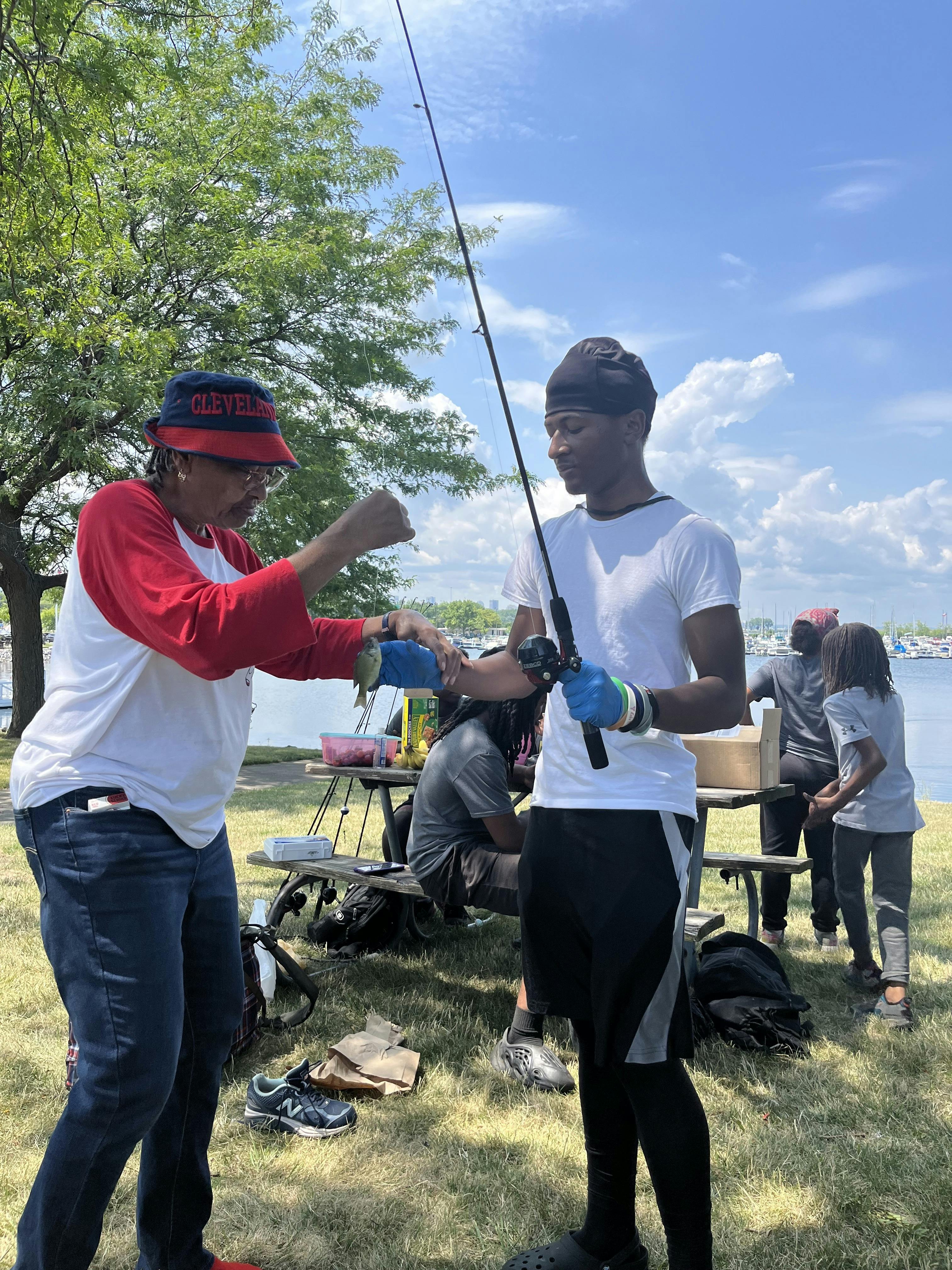 Person holding up a small fish to a person with a fishing rod