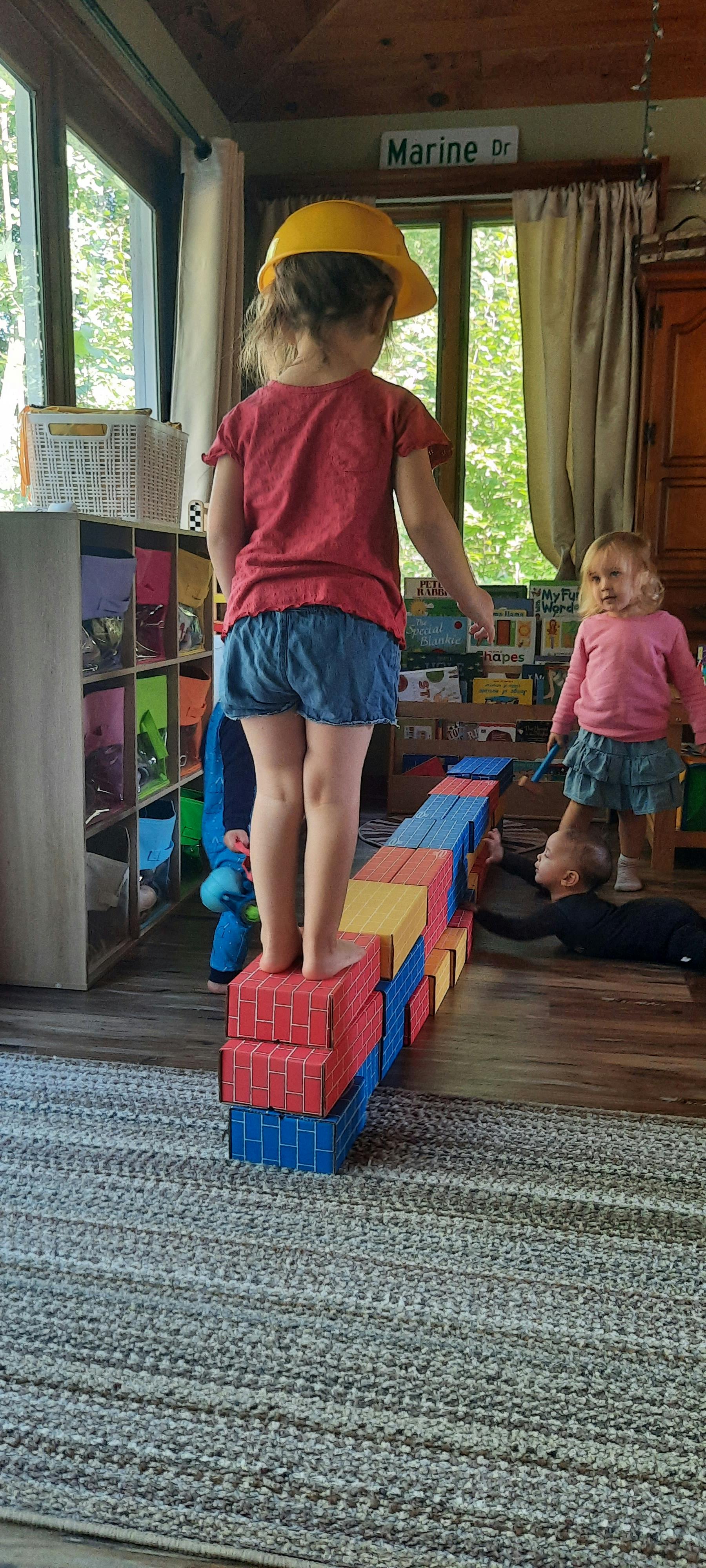 Child in a yellow hard hat standing on a block structure