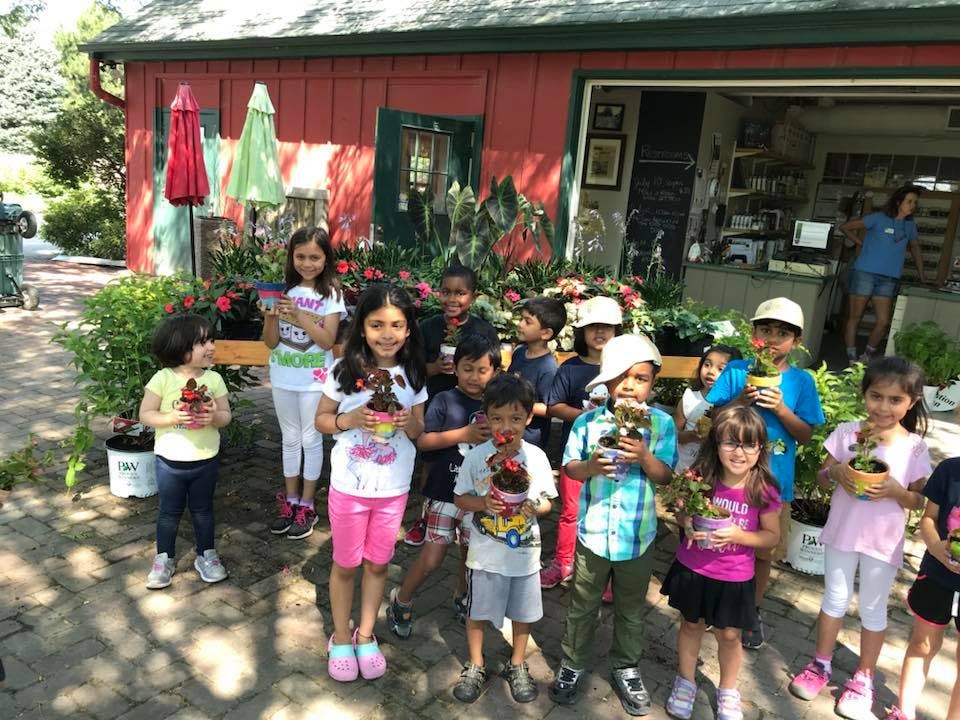 Group of children holding potted plants in front of a red building