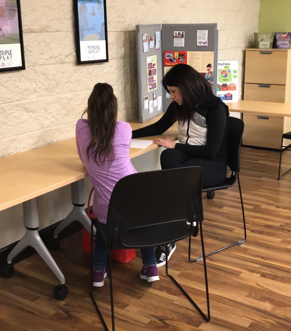 Two people sitting at a table, one writing on paper