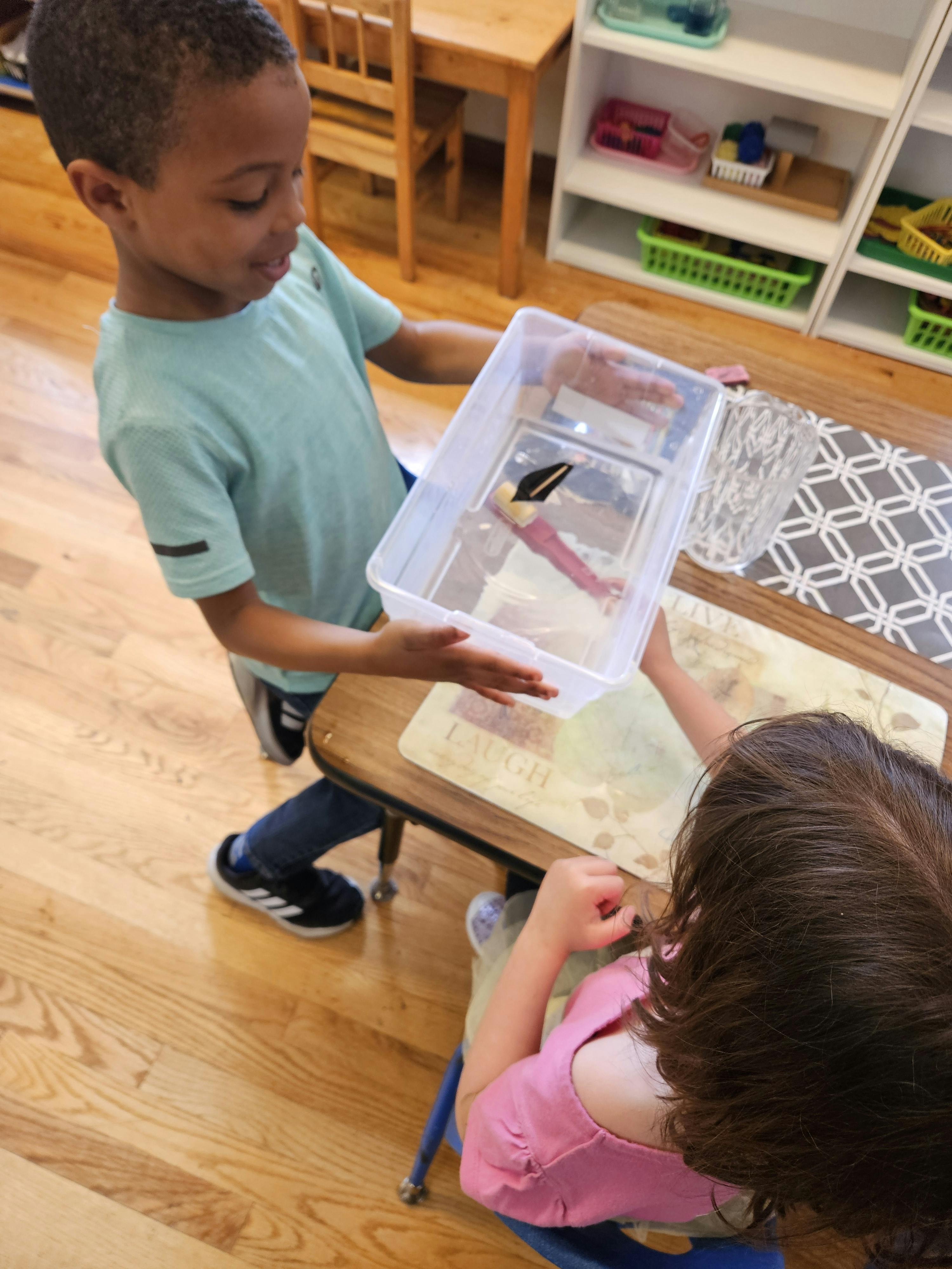 Child holding a clear container with a toy inside for another child