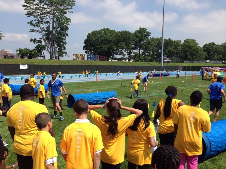 People in yellow shirts on a grassy field with blue tunnels and a track