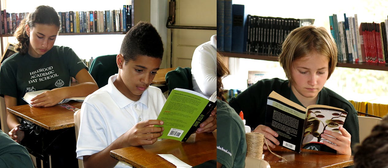 Three children reading books at desks in a classroom