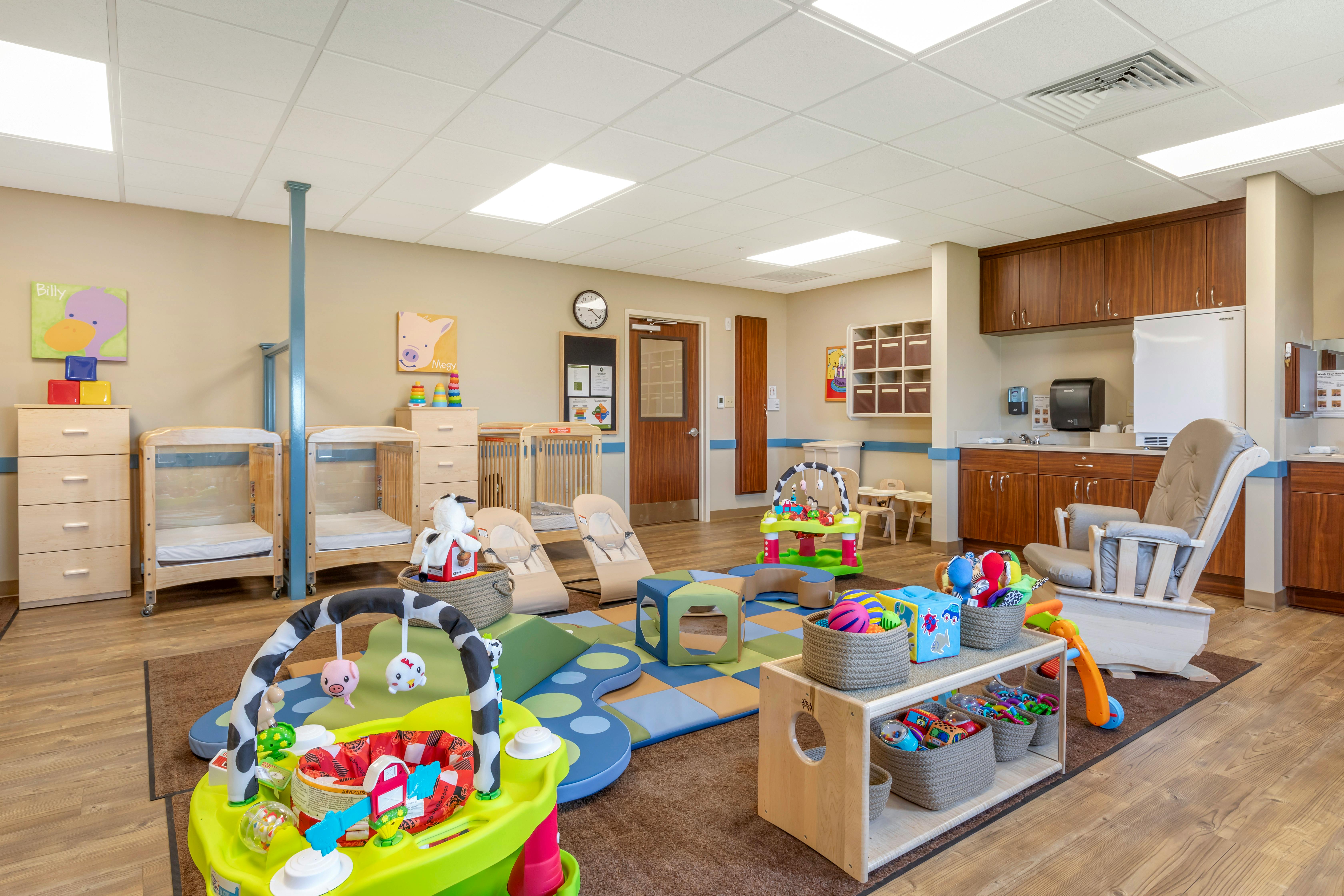 Infant and toddler room with multiple cribs, play mats, and toys