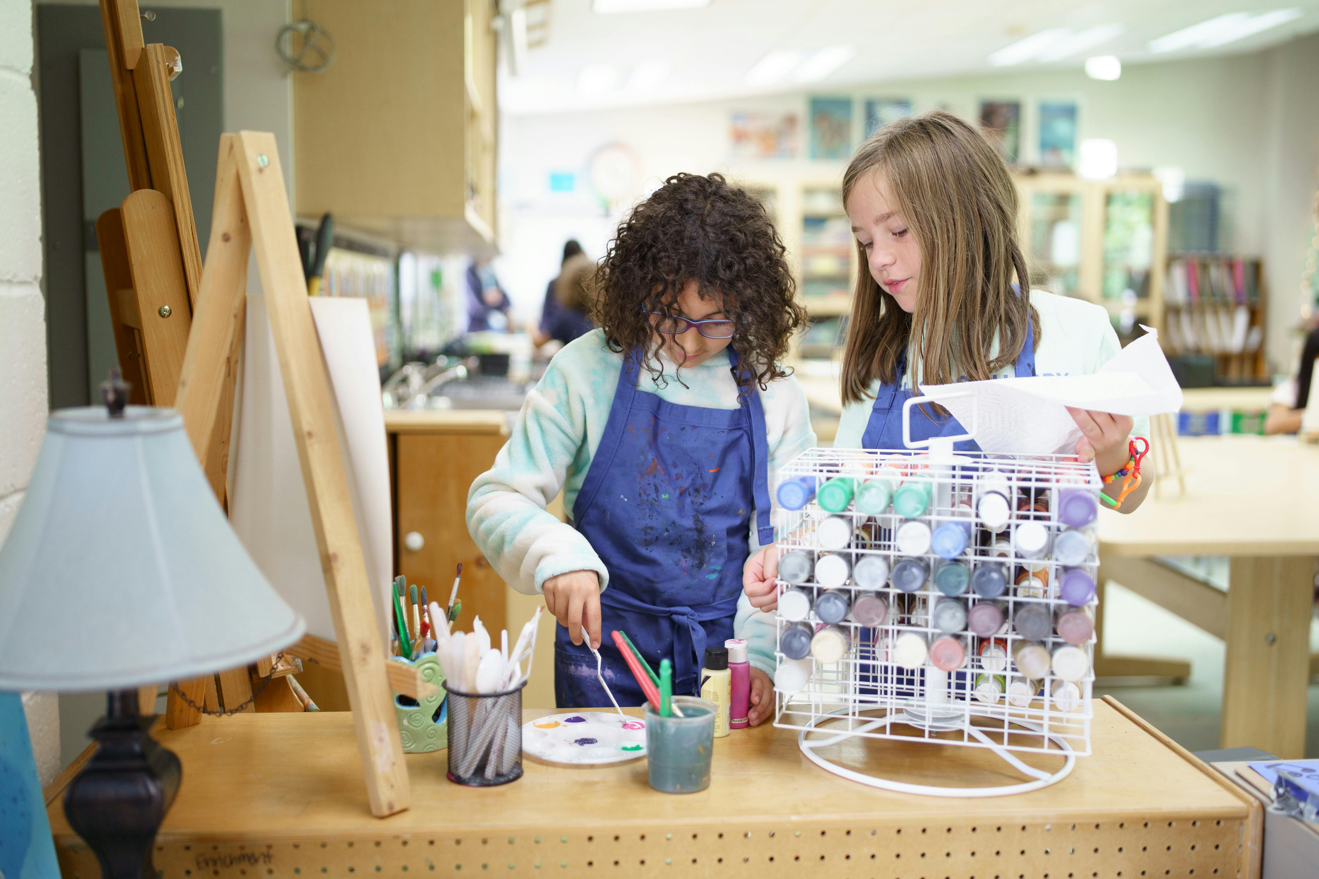 Two children in aprons painting in an art classroom