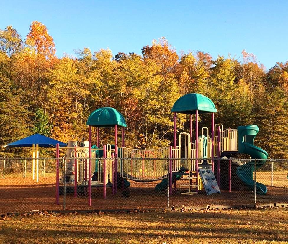 Playground with slides and climbing structures in front of autumn trees