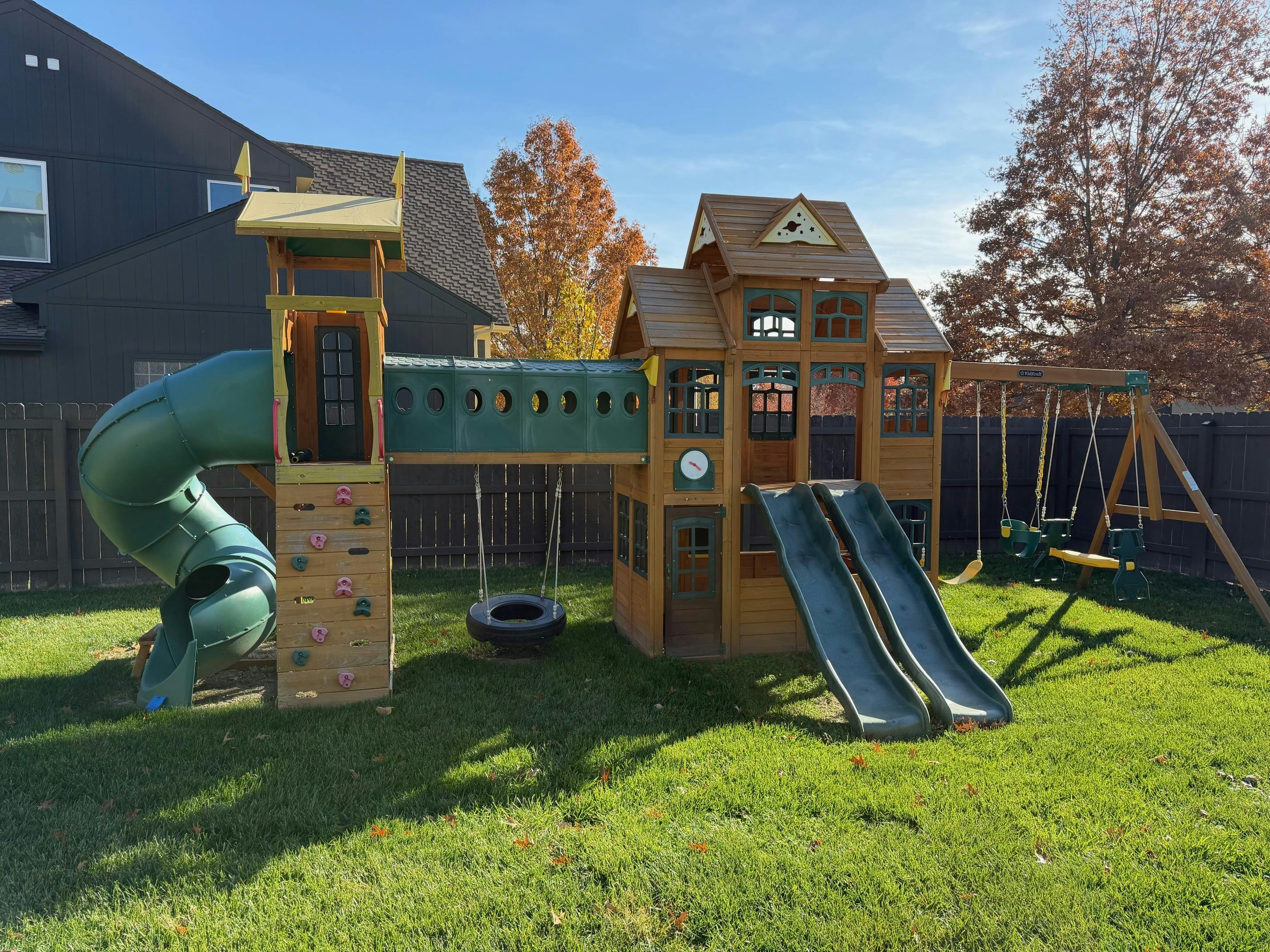 Large wooden playset with slides, swings, and climbing wall in a backyard