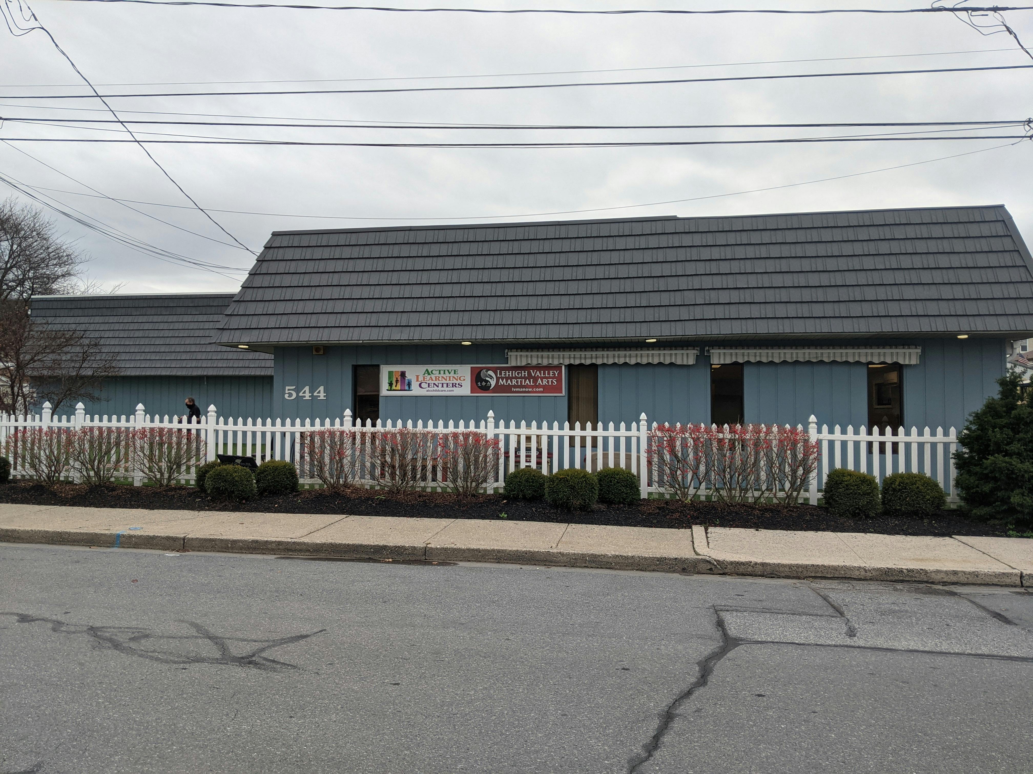 Light blue building with a dark gray roof and white picket fence
