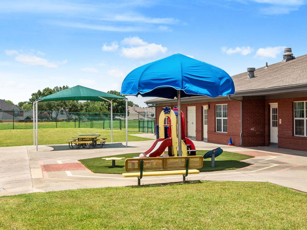 Outdoor playground with a blue umbrella covering a slide and a green canopy over a picnic table