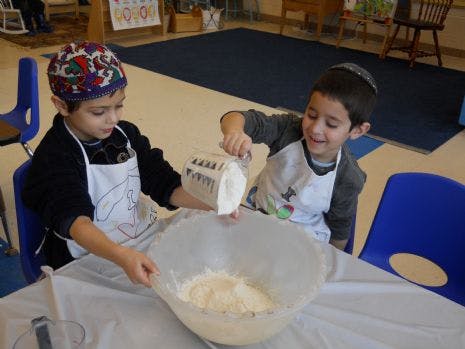 Two children in aprons pouring ingredients into a bowl