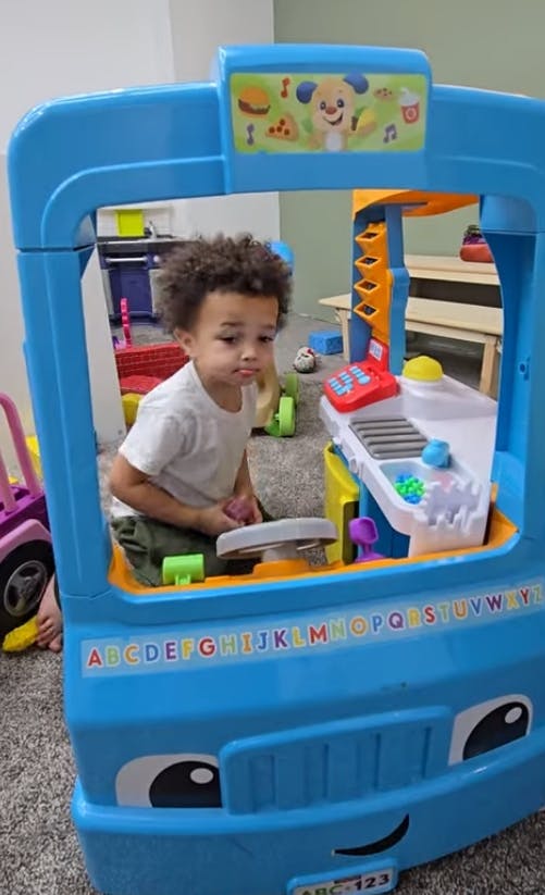 Child playing in a blue toy truck with a steering wheel and play kitchen