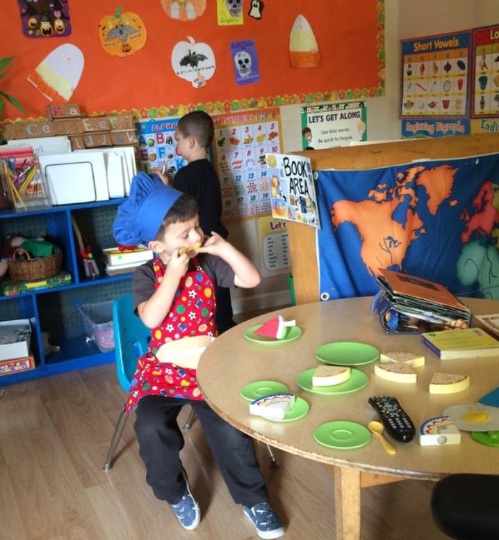 Child in chef hat and apron eating at a table with toy food