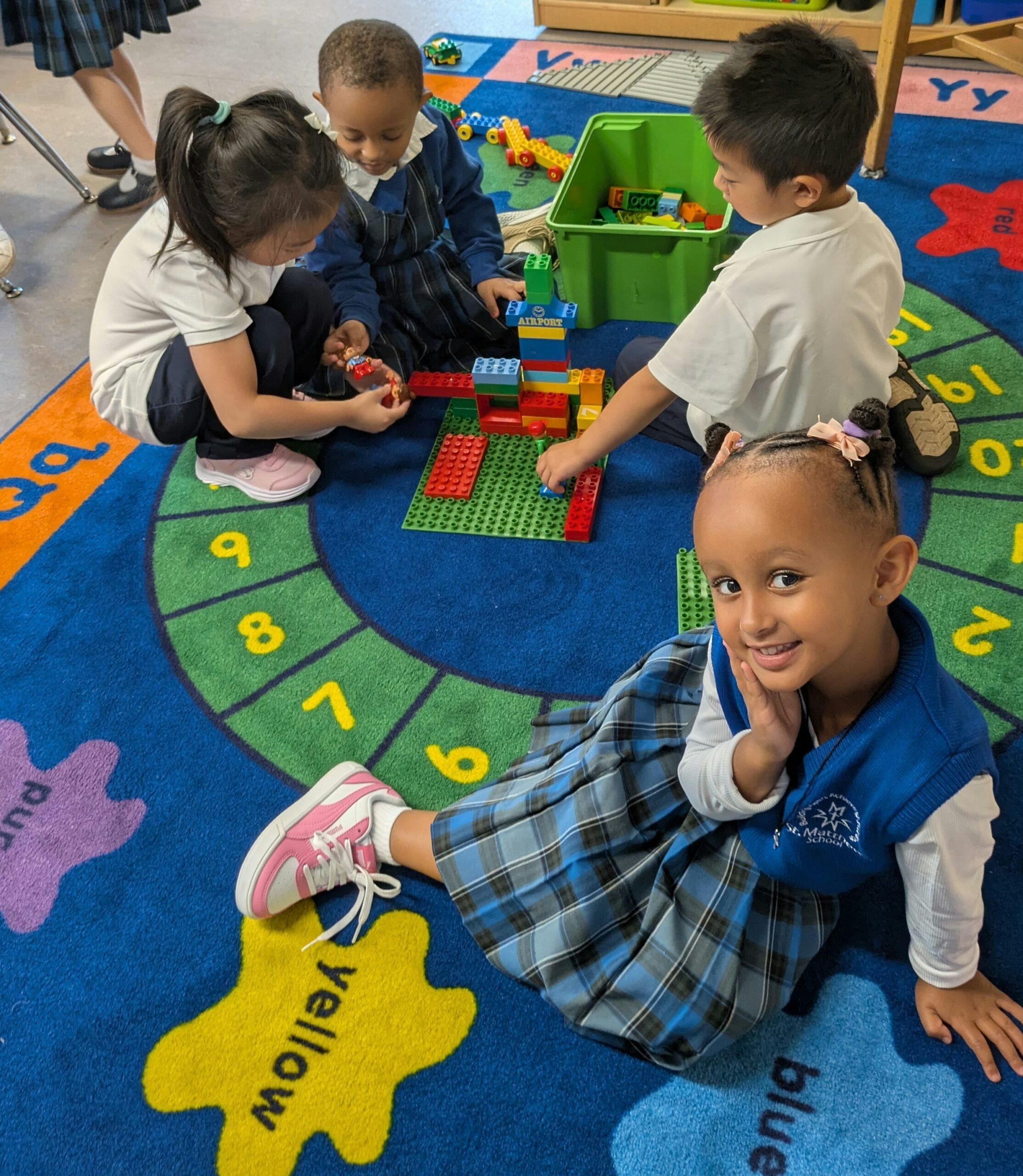 Four children playing with colorful building blocks on a numbered rug in a classroom