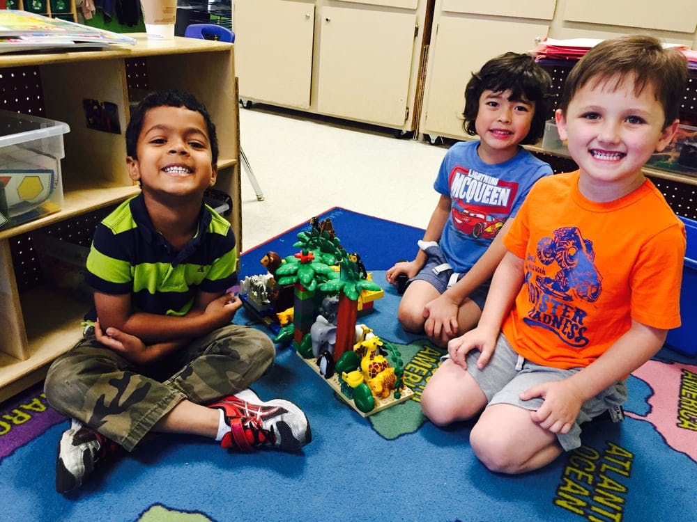 Three children sitting on a rug with a toy