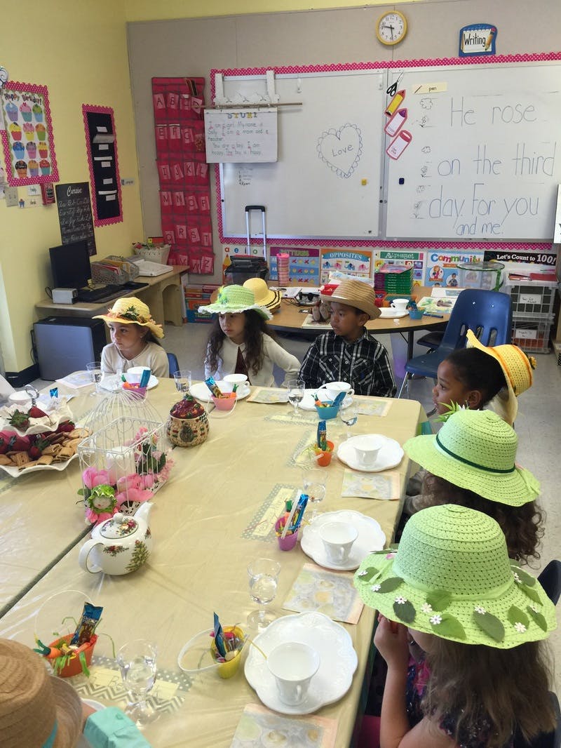 Children wearing hats at a table with teacups and snacks in a classroom