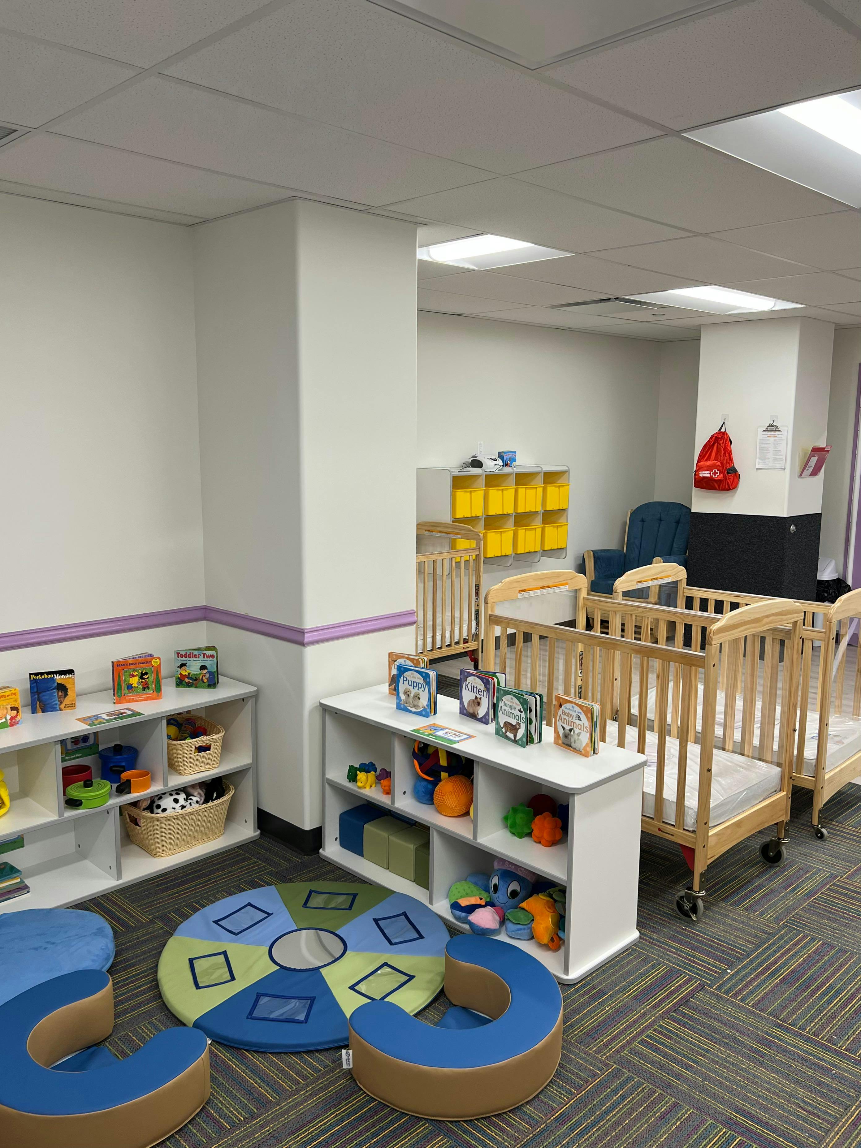 Nursery room with cribs, shelves of toys, and floor cushions
