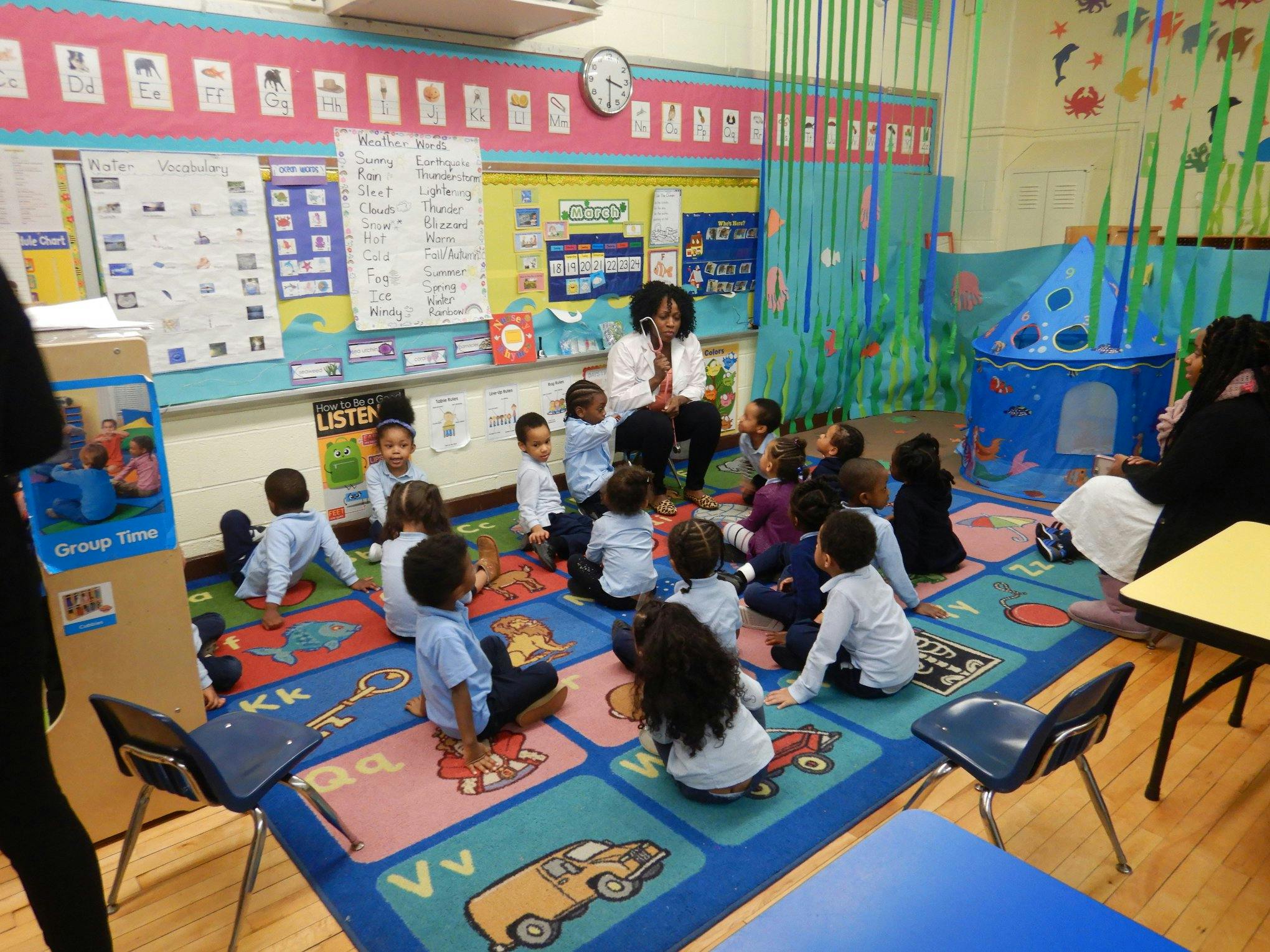 Adult leading a group of children sitting on a rug in a classroom
