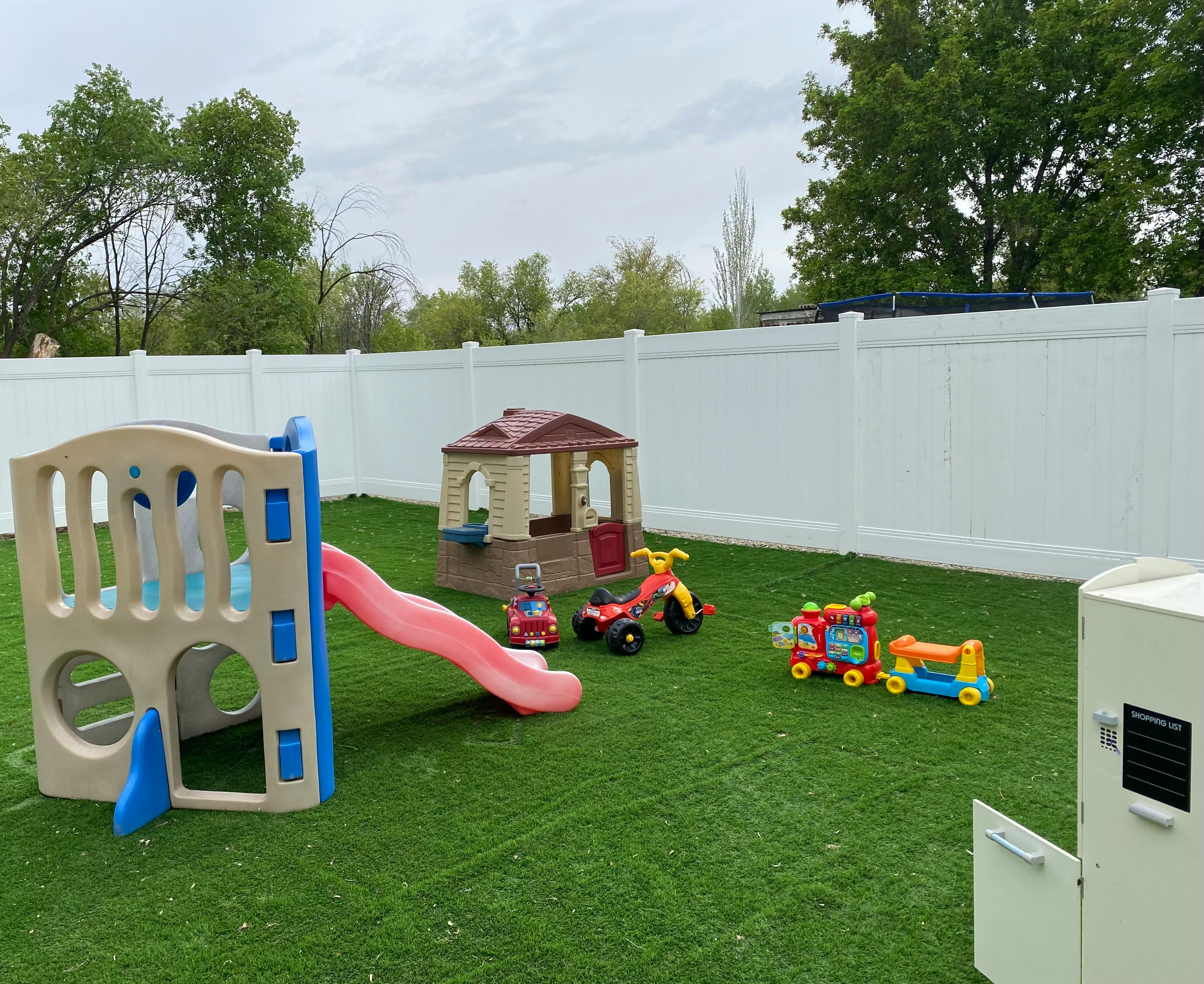Playground with slide, playhouse, and ride-on toys on artificial turf