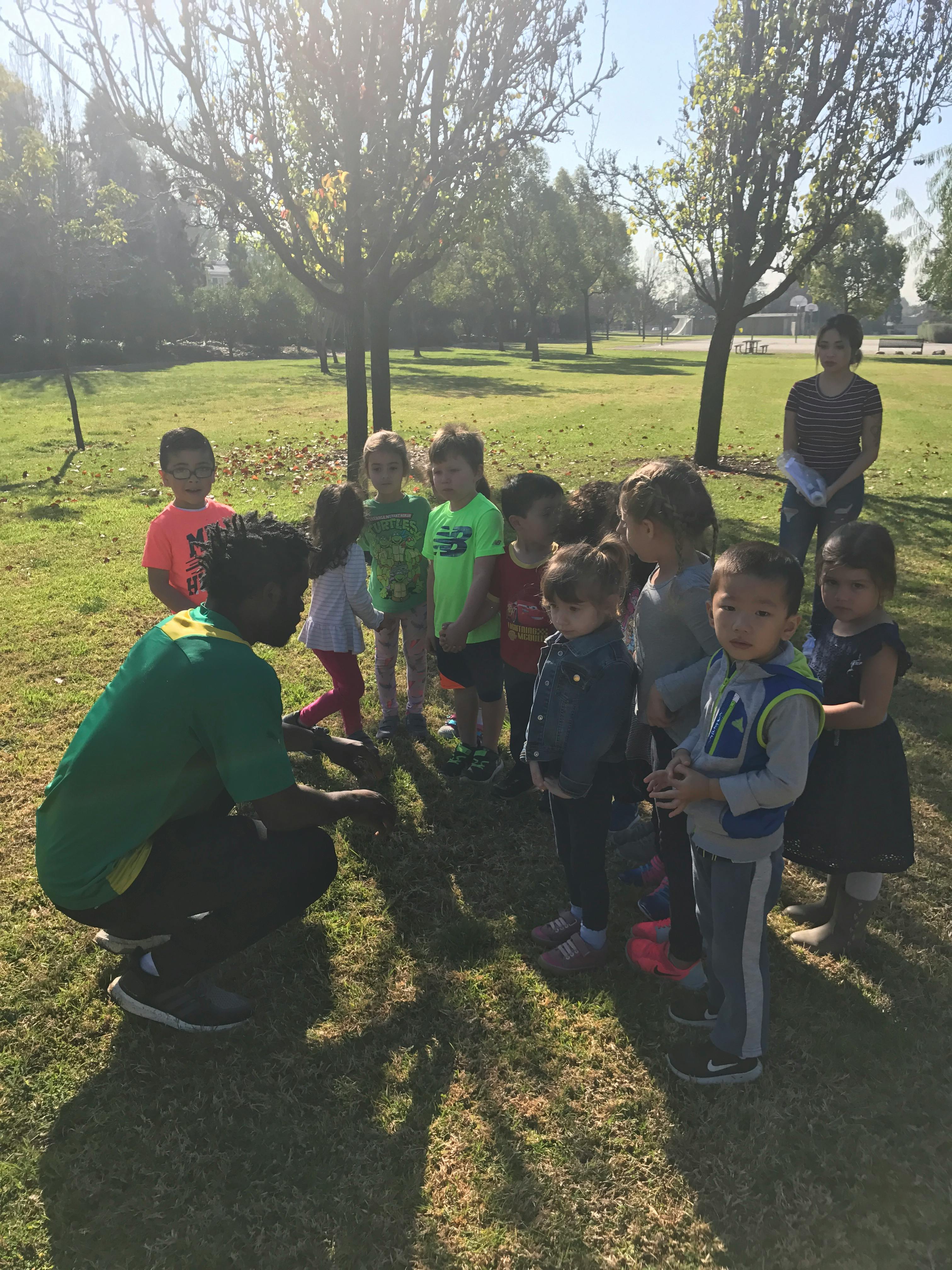 Person crouching with a group of children in a grassy area