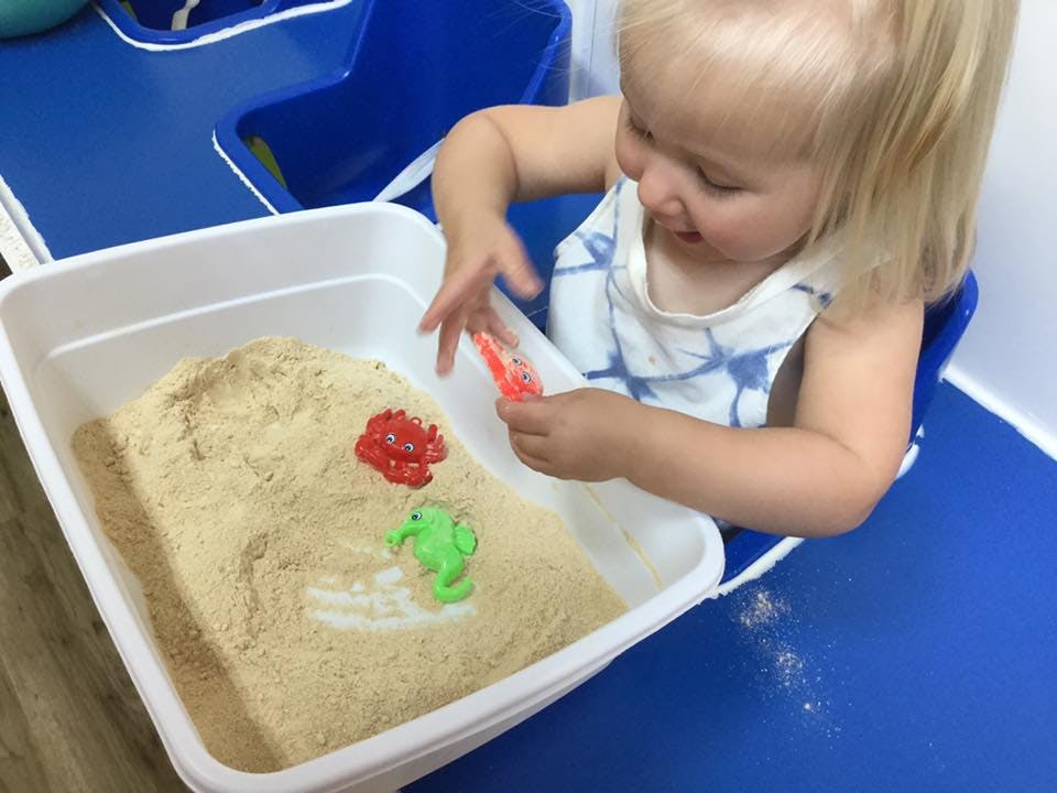 Child playing with sand and toys in a white bin