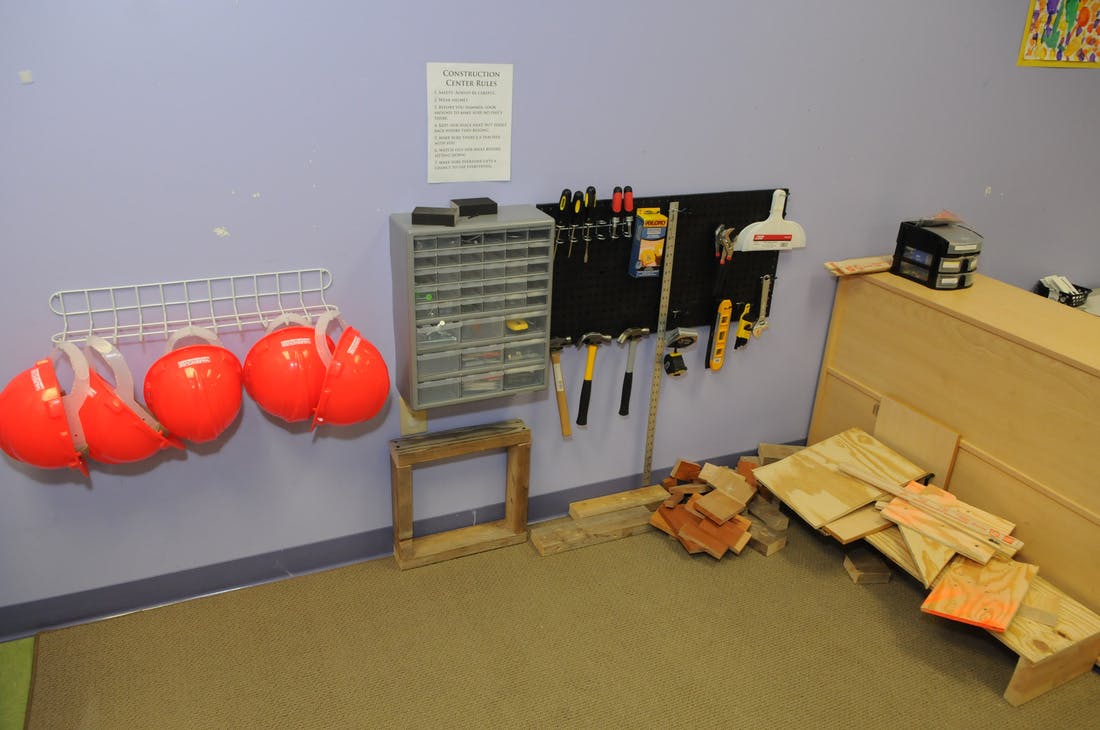 Three orange hard hats hanging on a wall next to a tool rack and wood storage area