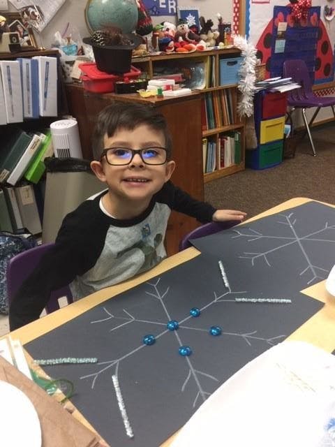 Child in glasses sitting at a desk with a snowflake craft