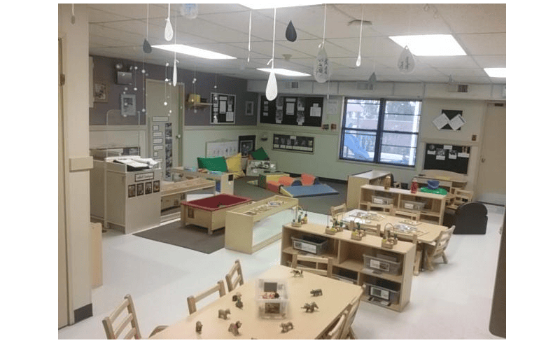 Classroom with small tables and chairs, play mats, and learning materials