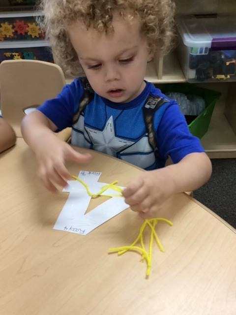 Child working on a craft with yellow pipe cleaners and a paper cutout