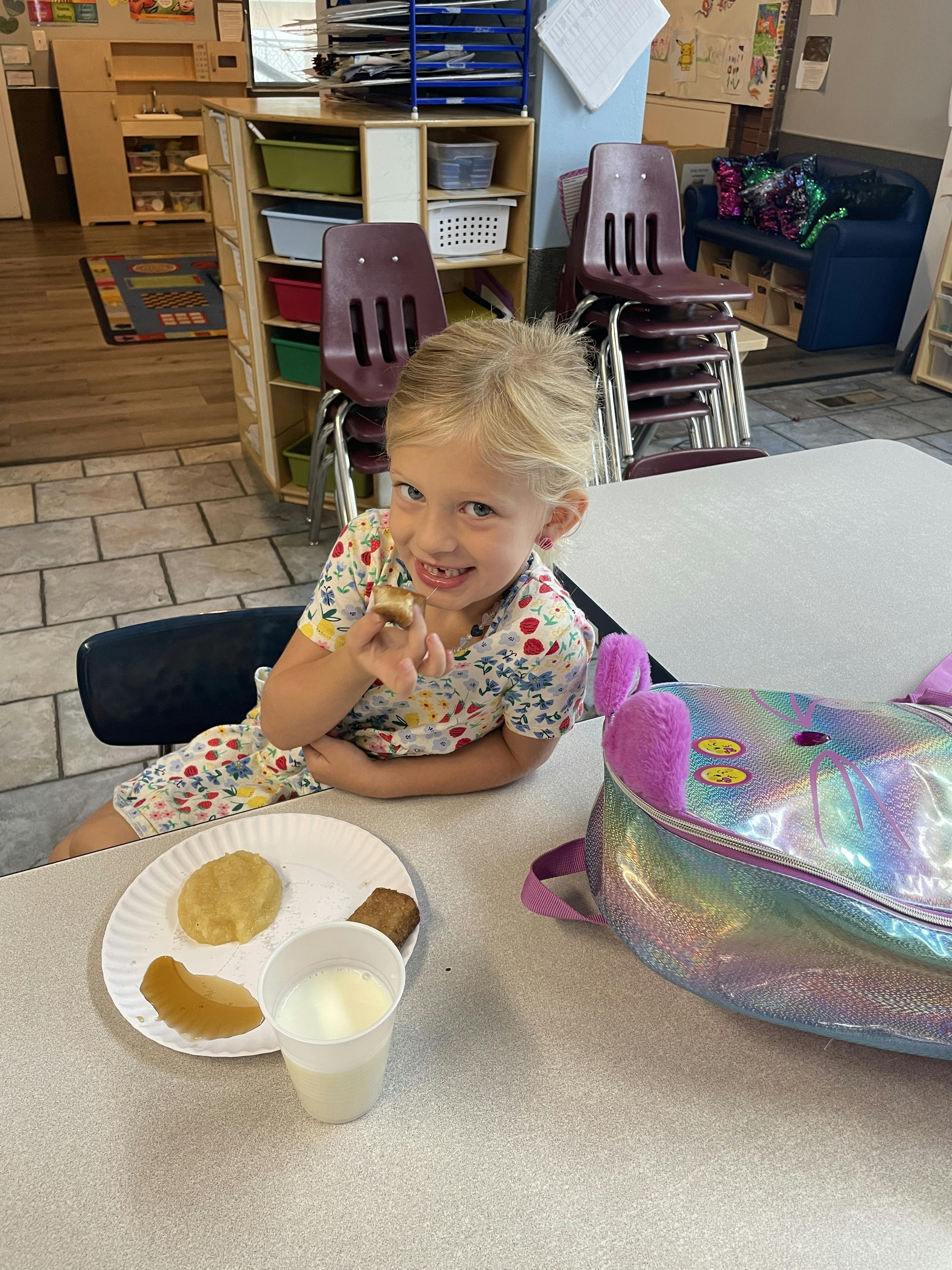 Child sitting at a table with a plate of food and a drink