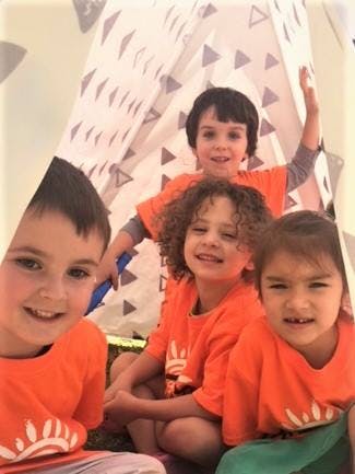 Four children in orange shirts in a tent