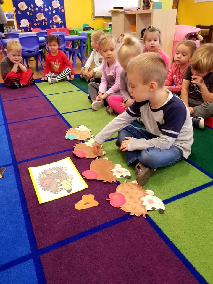 Children sitting on a colorful rug playing with cut-out shapes