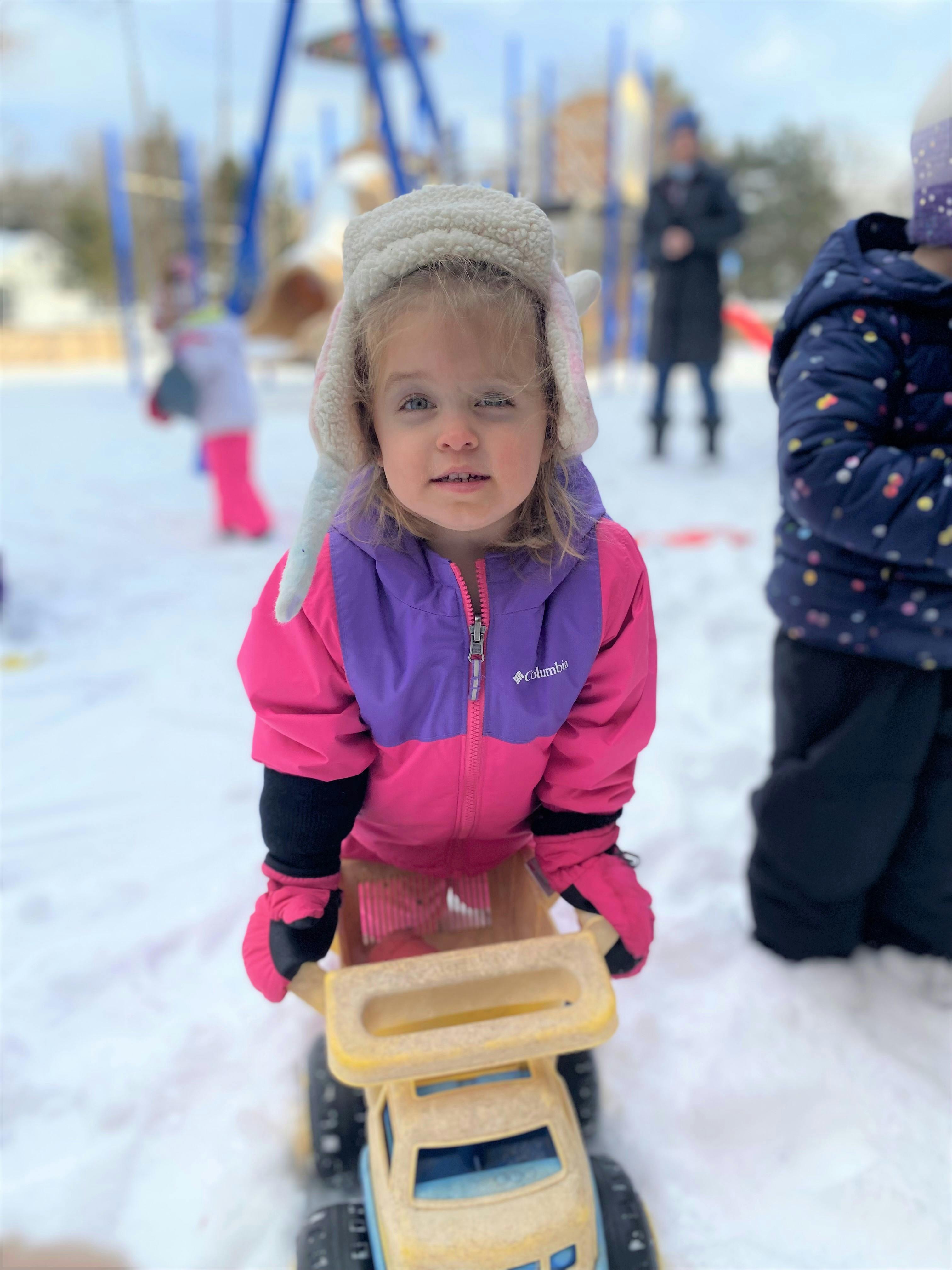 child in a winter coat and hat pushing a toy truck in the snow