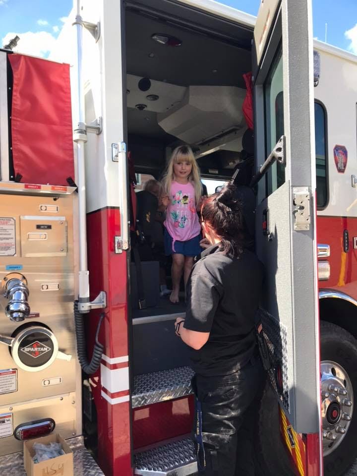 Child standing in a fire truck doorway with a person