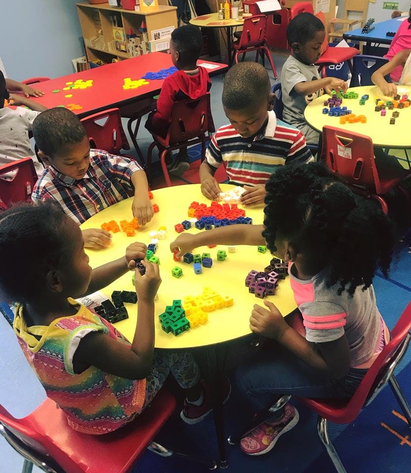 Children playing with colorful building blocks at a table in a classroom