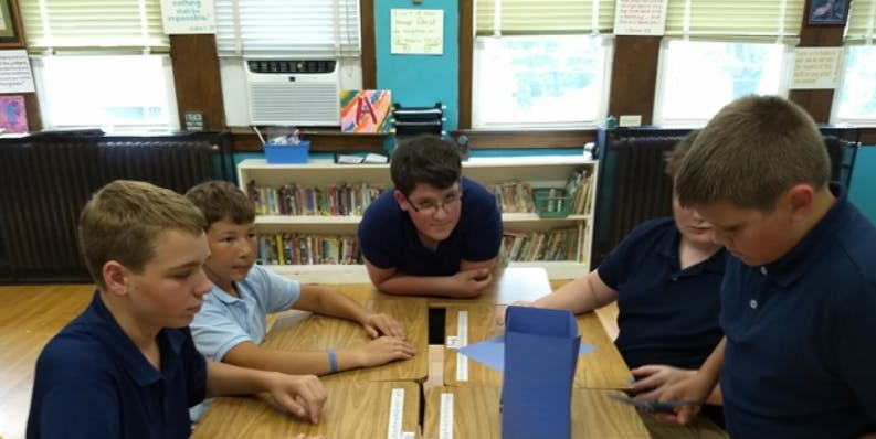 Four teens at a table with a blue paper structure