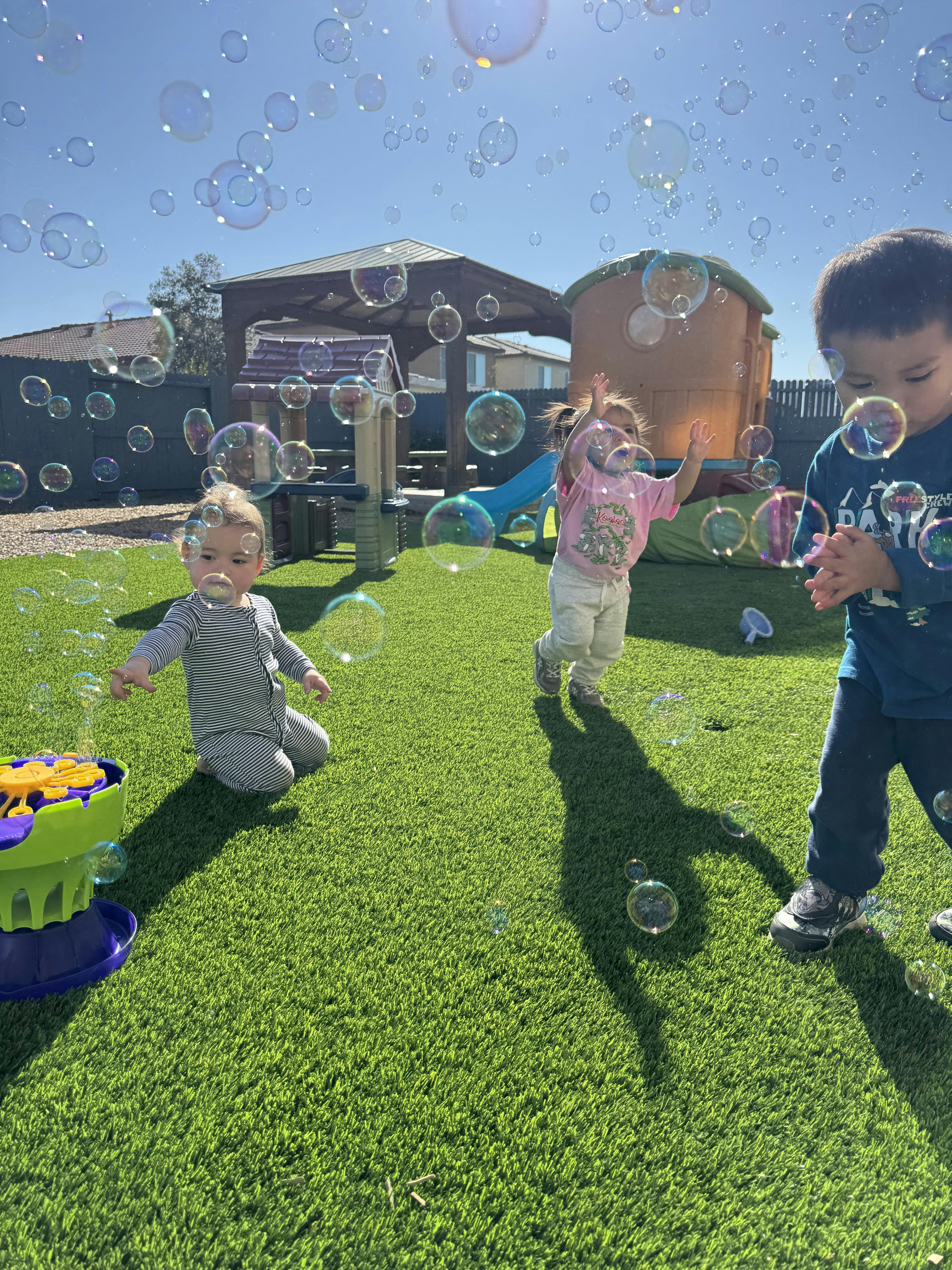 Three children playing with bubbles on green turf