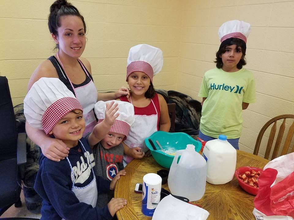 Adult and children in chef hats and aprons around a table with cooking ingredients