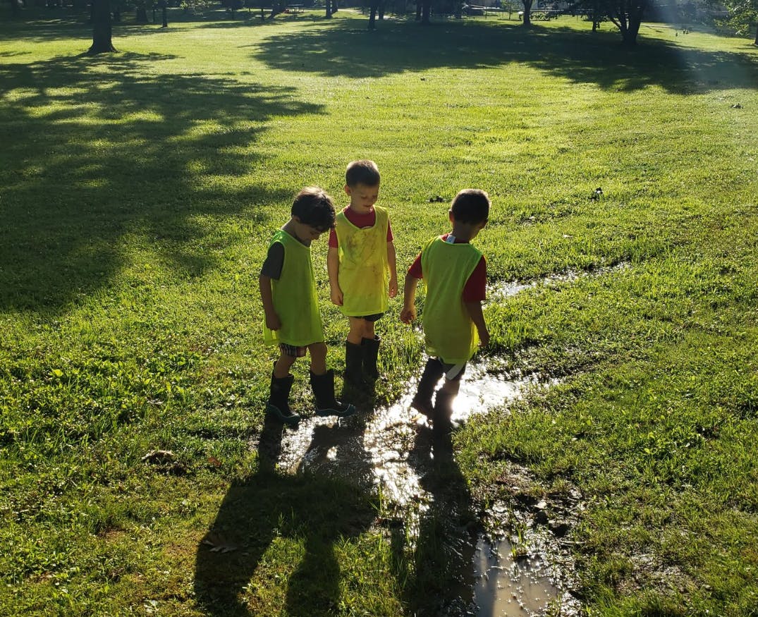 Three children in boots standing in a muddy puddle
