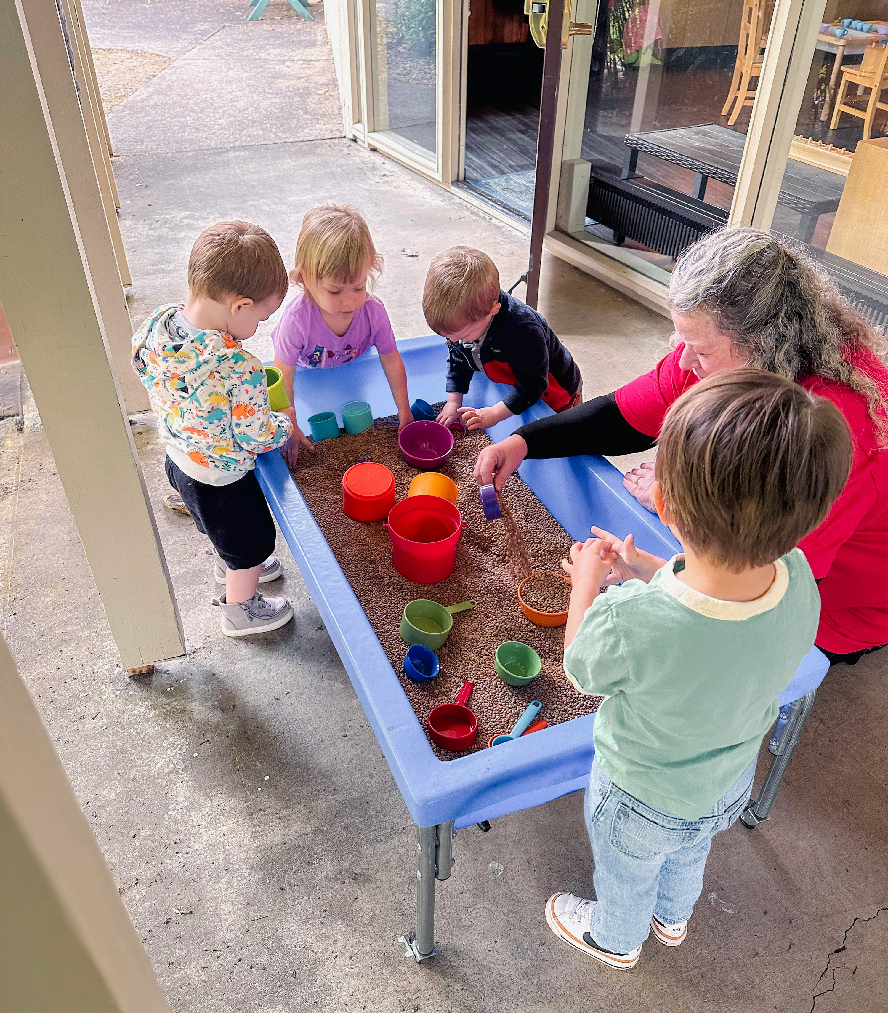 Adult and three children playing in a sand table with colorful toys
