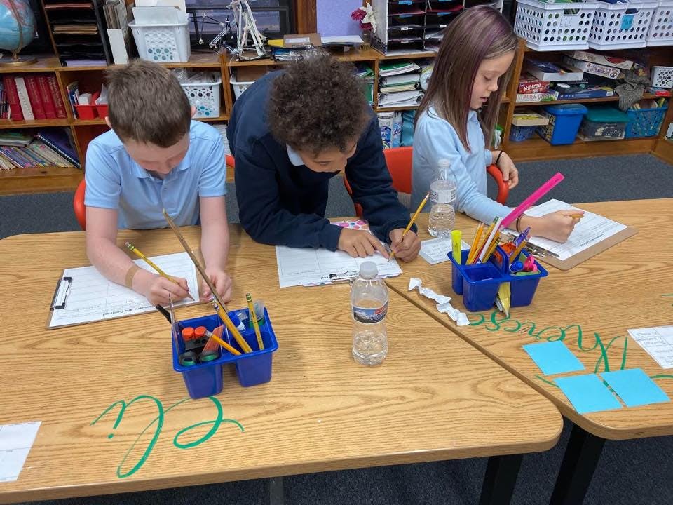 Three children writing at desks in a classroom