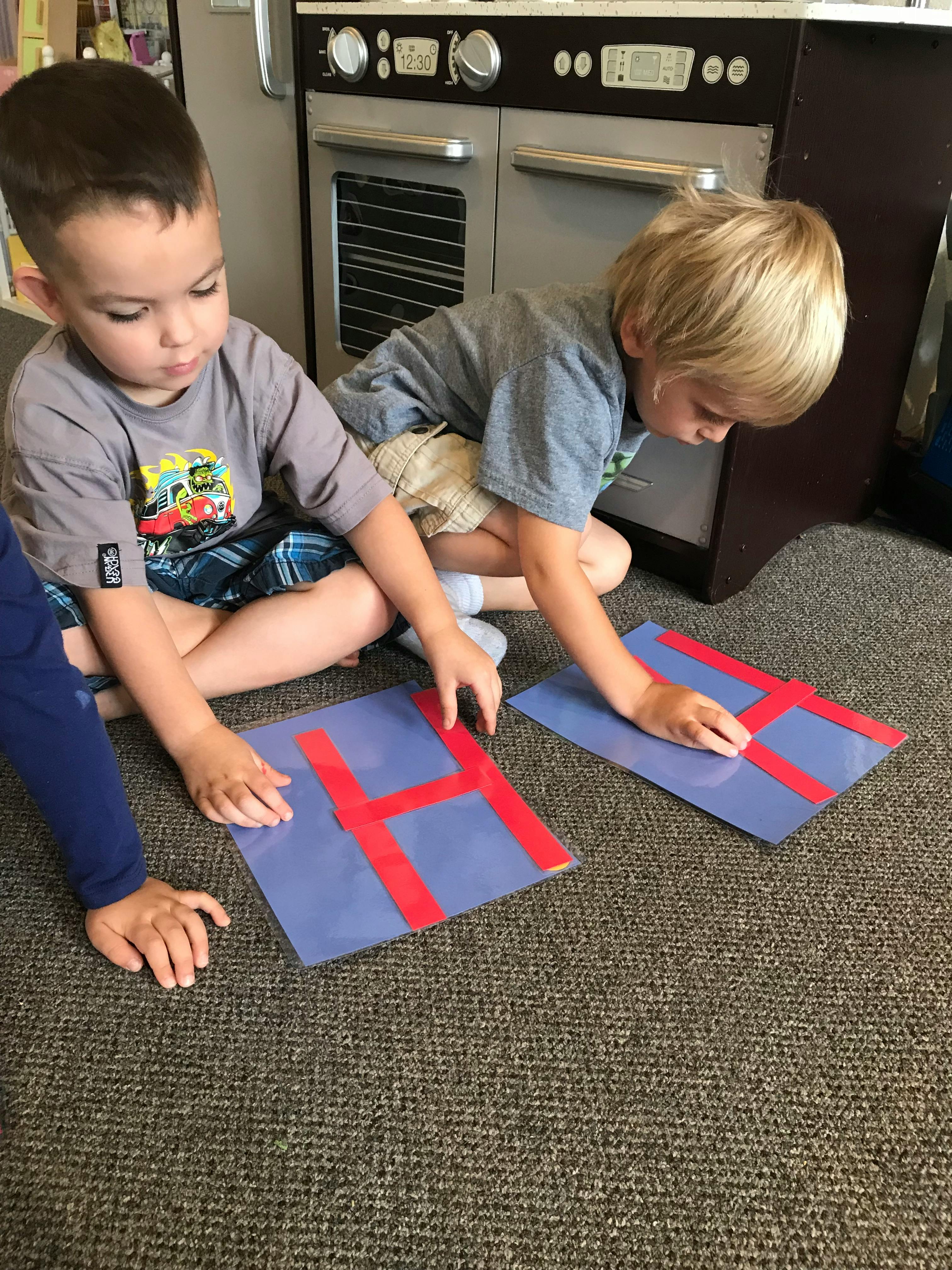 Two children sitting on the floor assembling letter H shapes