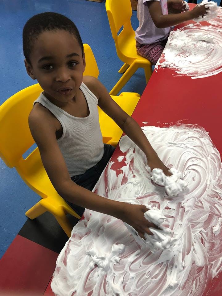 Child playing with shaving cream on a red table
