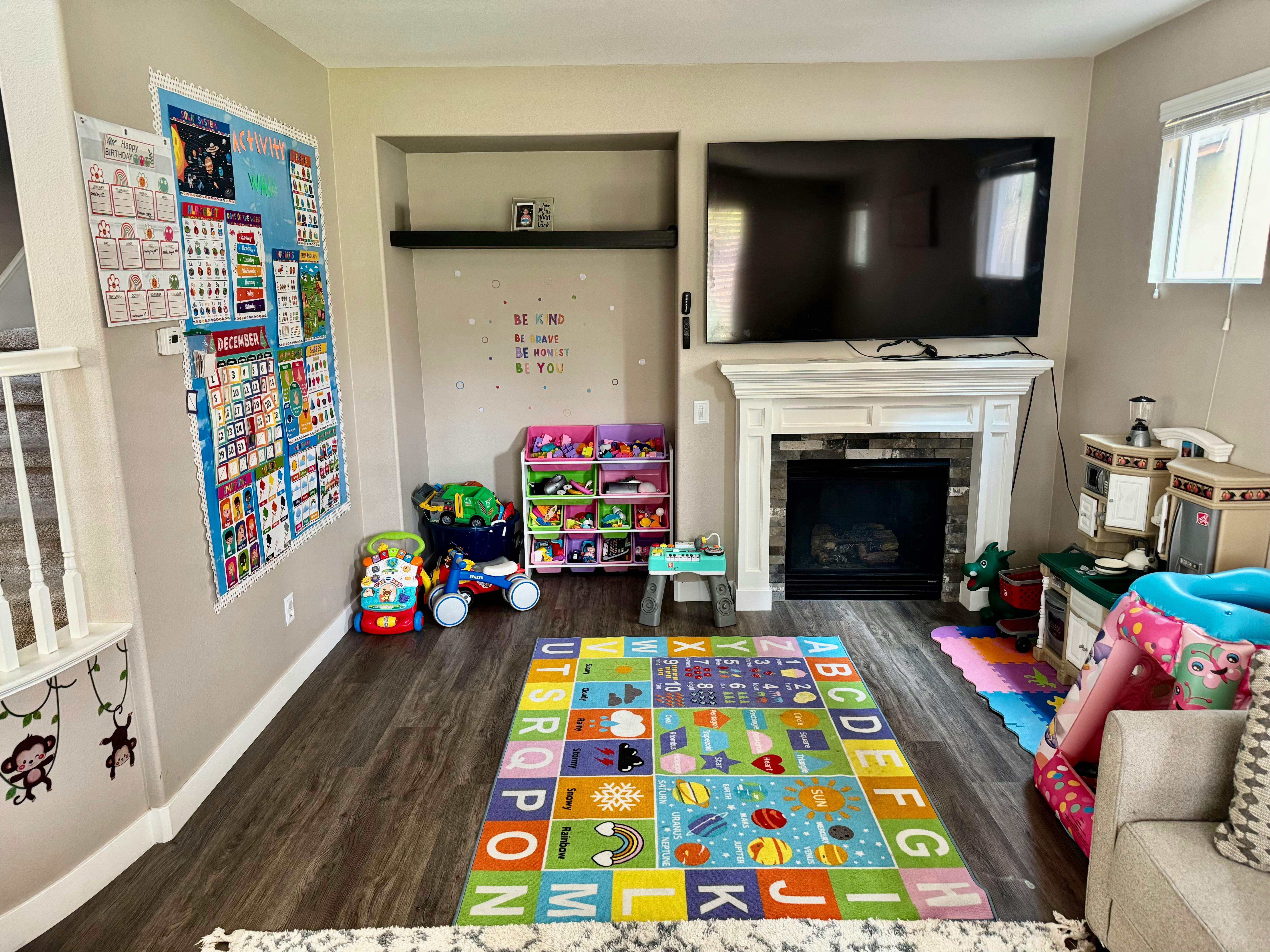 Living room with a colorful alphabet rug, fireplace, and wall-mounted TV