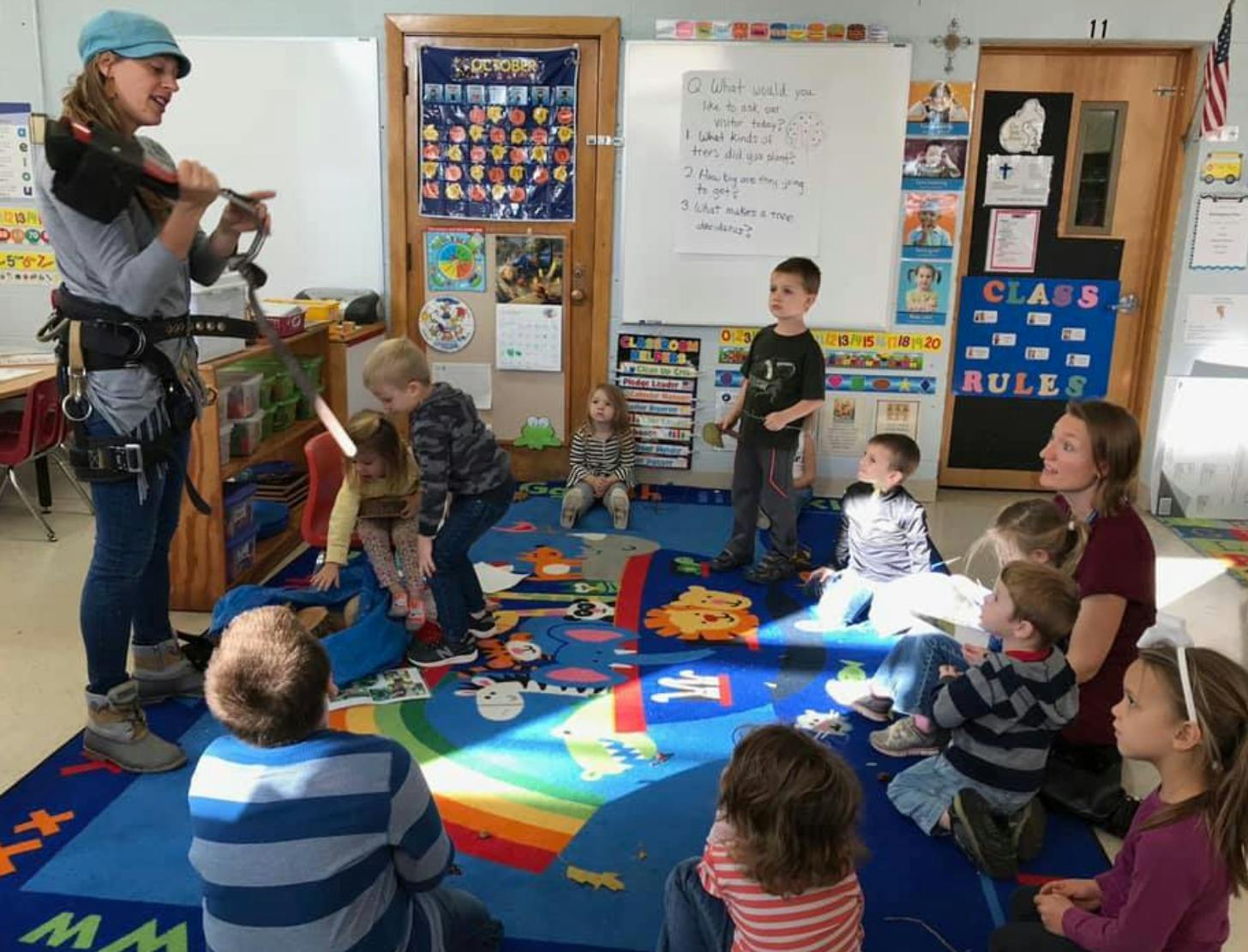 Person in climbing harness talking to children in a classroom
