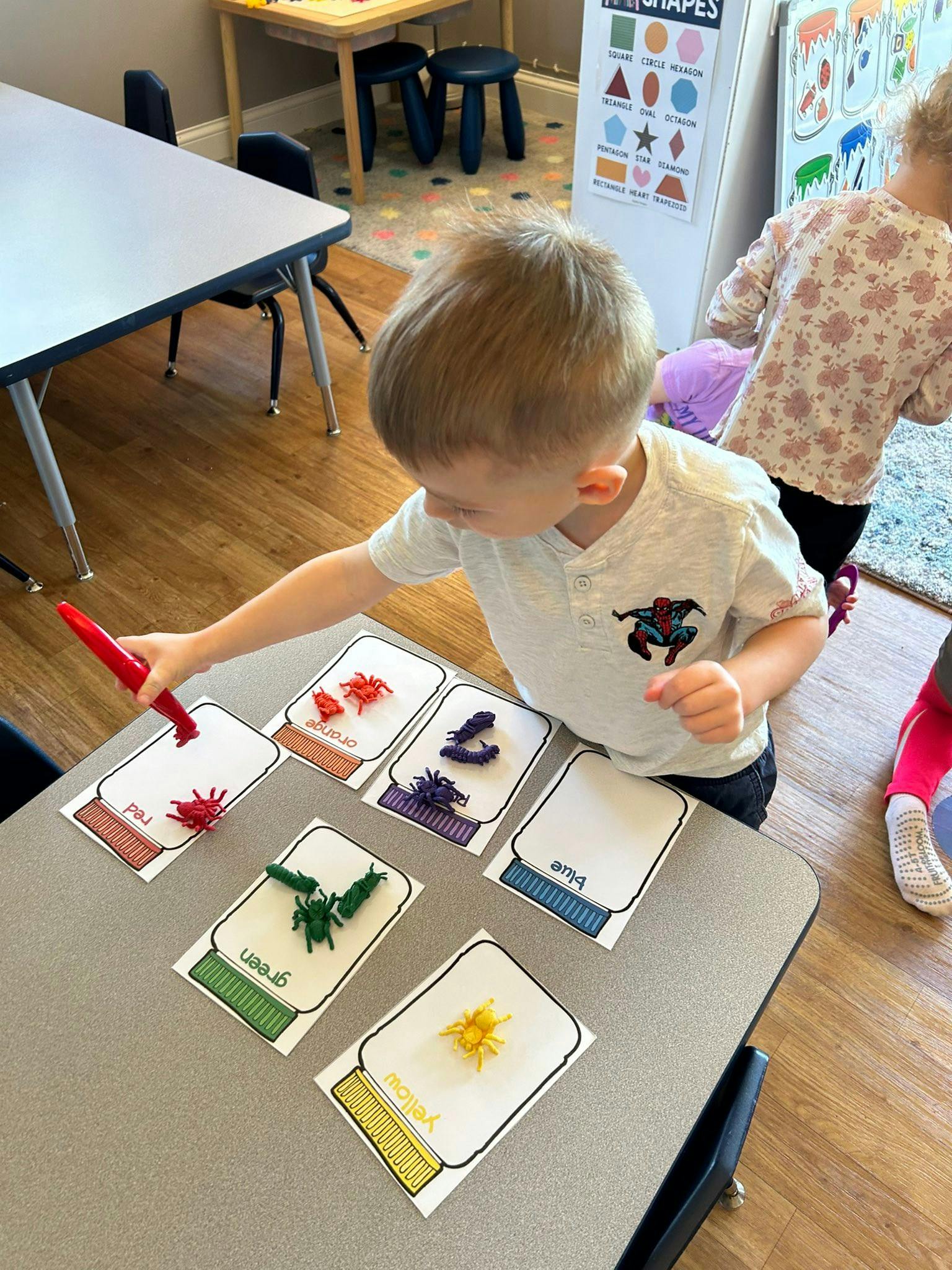 Child placing plastic spiders on color-coded jar cards at a table